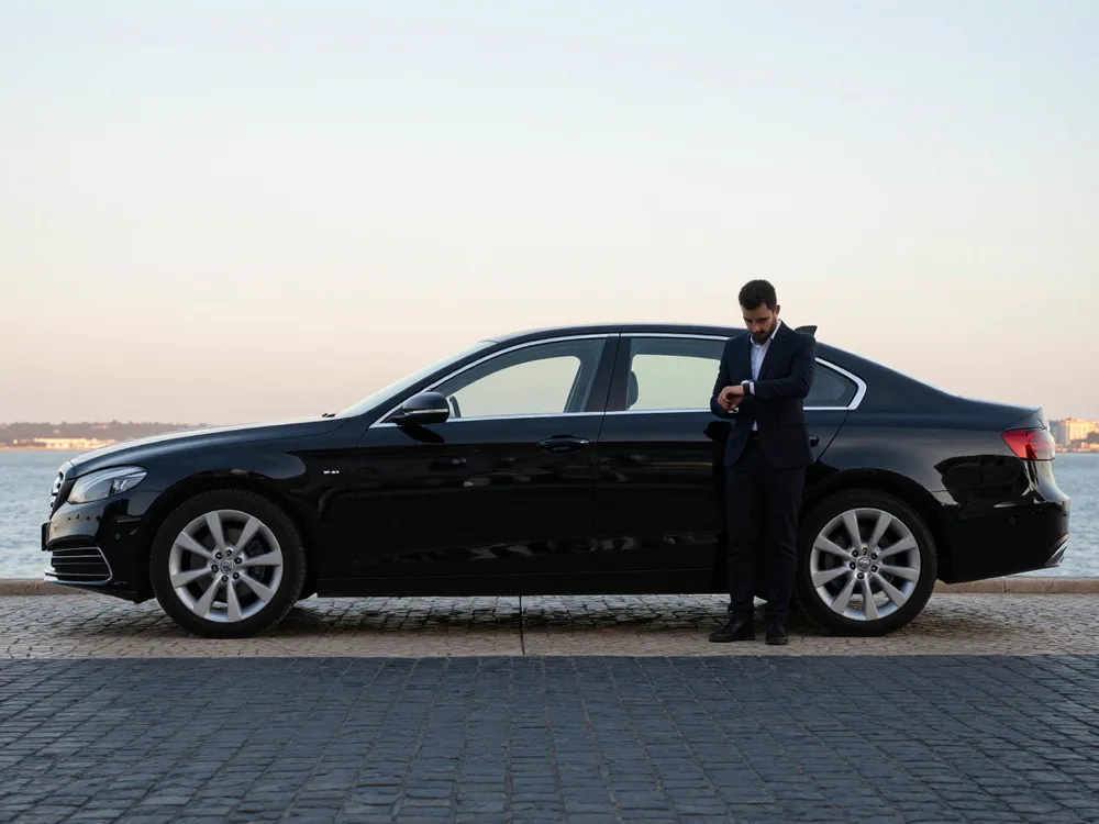 Chauffeur checking his watch beside a black sedan