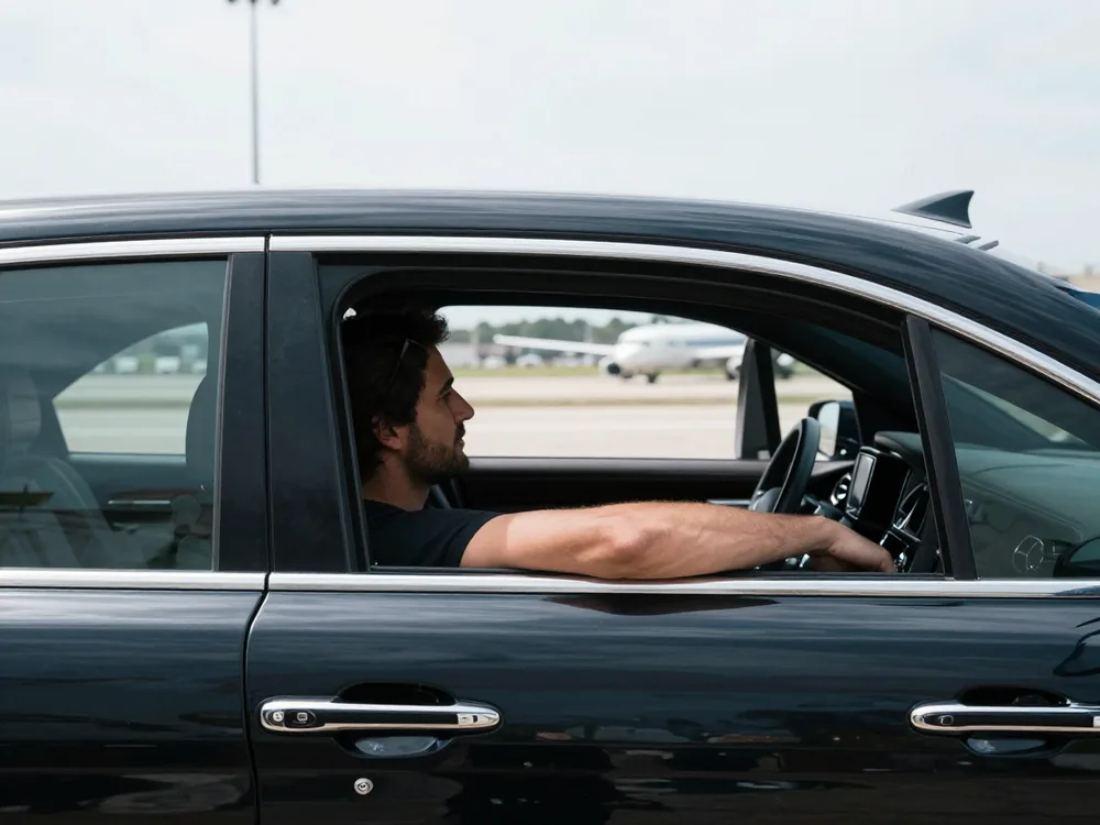 Traveller checking a fixed fare on a phone beside a sedan