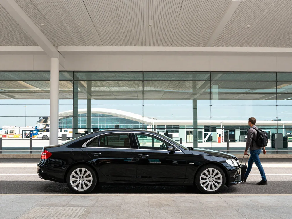 Black sedan at the airport kerb as a traveller walks up with his suitcase