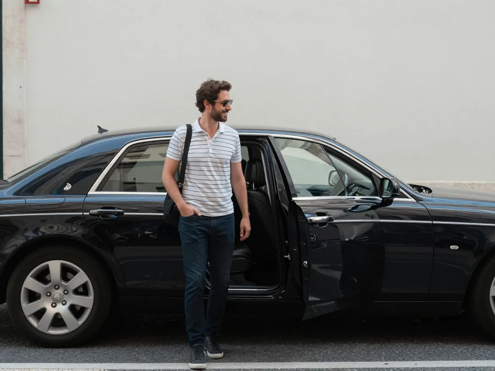 Traveller reading a booking confirmation beside a waiting sedan